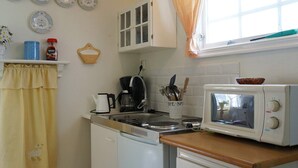 A compact kitchen with a white stove, a microwave, and a coffee maker. There are decorative plates on the wall and a window with a curtain. - 5 Person Holiday Home in Fiskebackskil-by Traum (Fiskebackskil)
