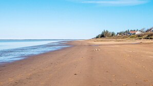 A wide sandy beach with a calm sea, a clear sky, and houses in the background. - 4 Person Holiday Home in Esbjerg V (Esbjerg)