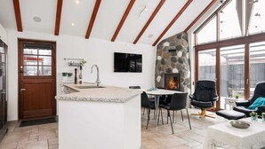 A modern kitchen with a stone accent wall, a dining area with a fireplace, and a cozy seating area with a view of the outdoors. - 4 Person Holiday Home in Esbjerg V (Esbjerg)
