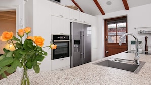 A modern kitchen with white cabinetry, stainless steel appliances, a granite countertop, and a wooden ceiling beam. - 4 Person Holiday Home in Esbjerg V (Esbjerg)