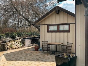 A patio area with a wooden table and two chairs, a stone wall, and a potted plant.