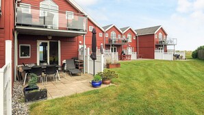 A row of red houses with balconies, a patio area with outdoor furniture, and a well-maintained lawn. - 6 Person Holiday Home in Hadsund (Hadsund)