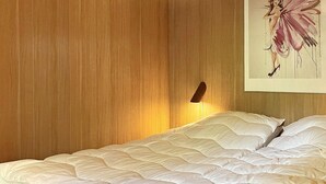 A neatly made bed with white bedding in a room with wooden paneling and a wall-mounted light fixture. - 4 Person Holiday Home in Aakirkeby (Akirkeby)
