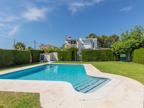 A swimming pool with a curved edge, surrounded by a well-maintained lawn and a hedge.