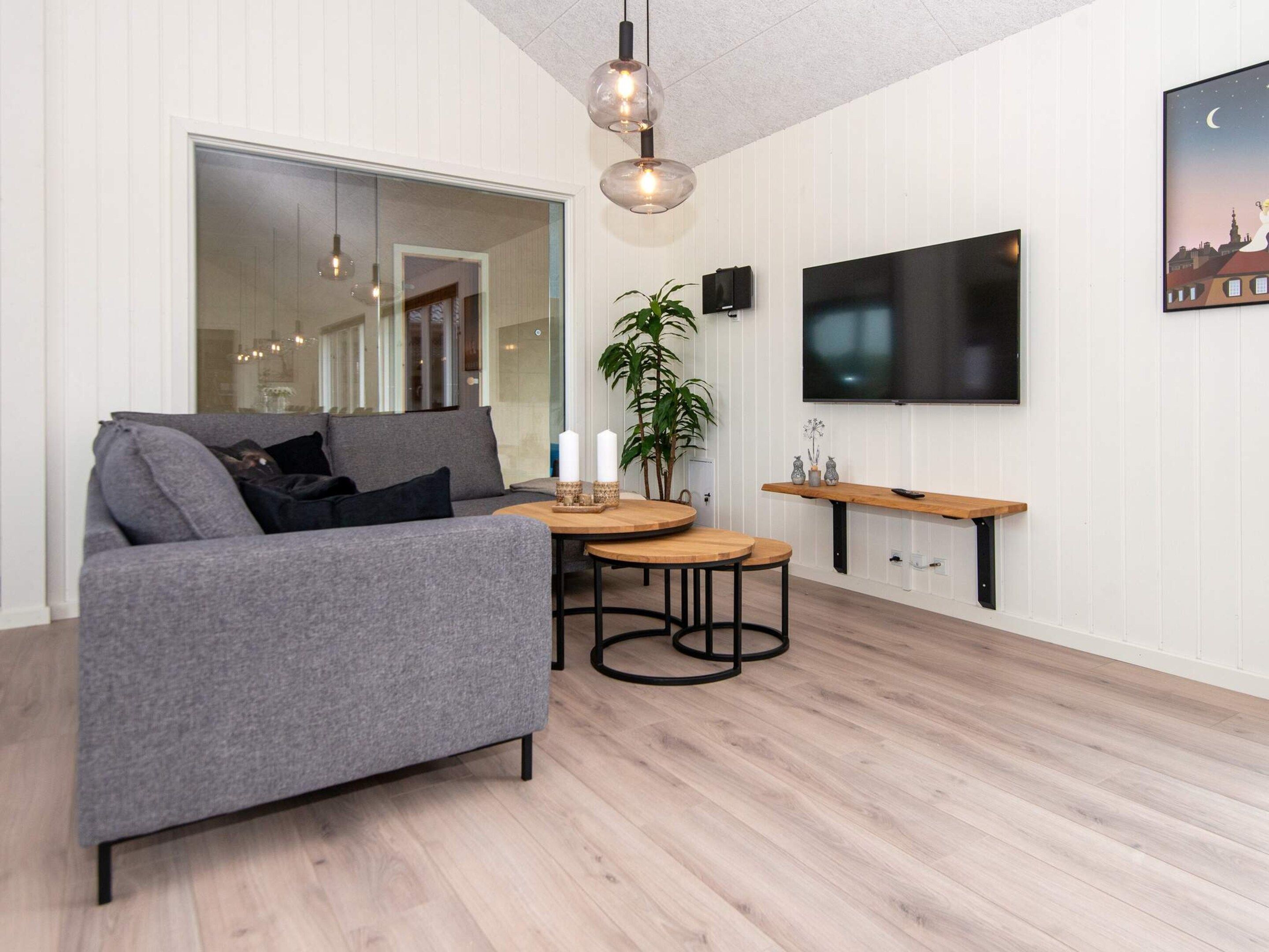Ein modernes Wohnzimmer mit einem grauen Sofa, einem Holztisch und einem an der Wand montierten Fernseher.