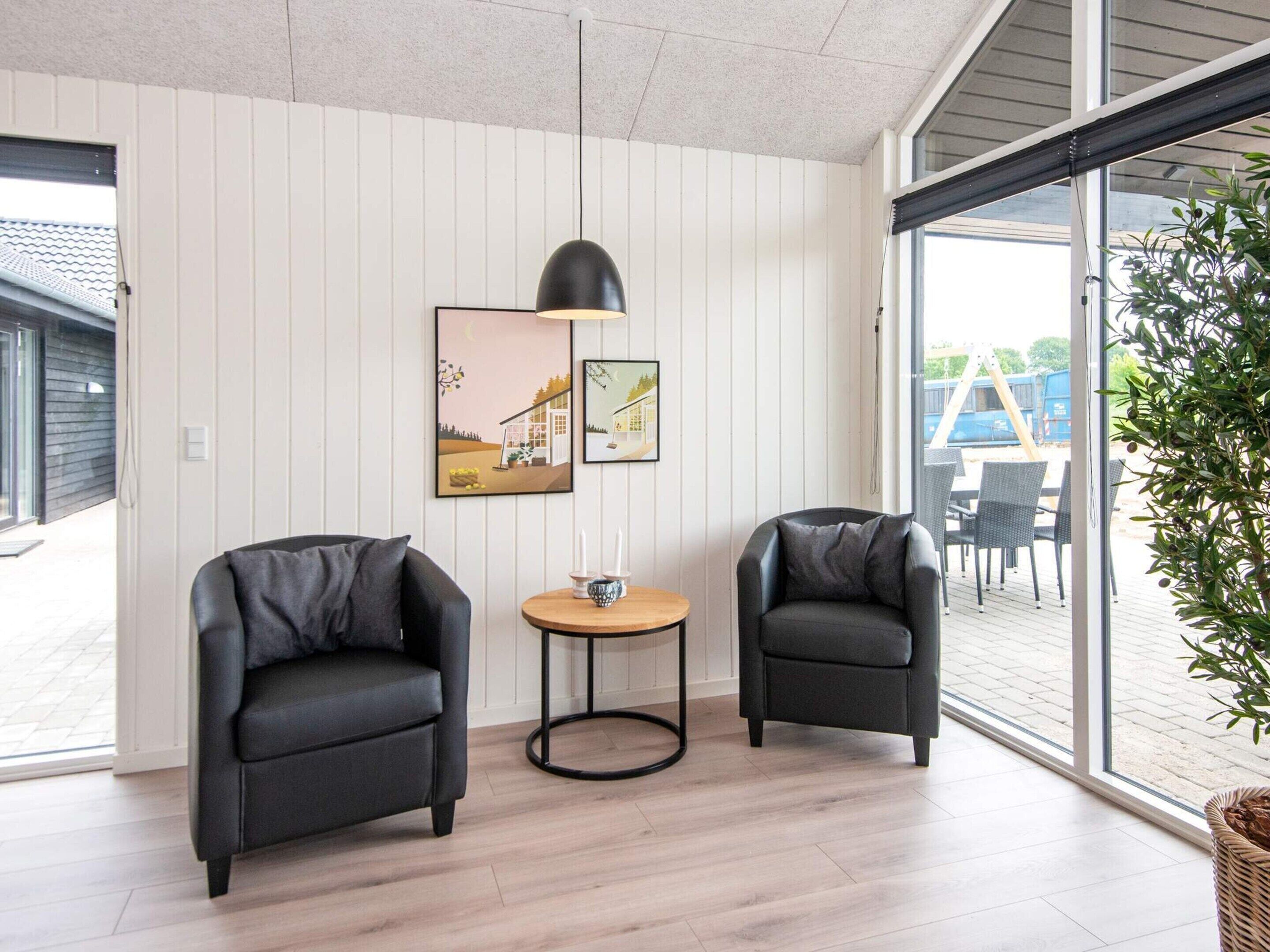 Ein modernes Zimmer mit zwei schwarzen Sesseln, einem kleinen runden Tisch und einer Pendelleuchte. An der Wand befinden sich zwei gerahmte Bilder.
