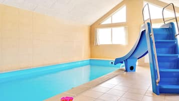 An indoor swimming pool with a blue slide and stairs, tiled walls, and a window.
