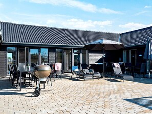 Un patio exterior con una parrilla, zona de estar y sombrillas cubiertas.