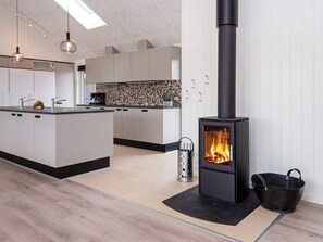 Una cocina moderna con una isla central, una estufa de leña negra y una lámpara colgante.