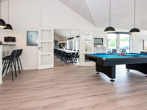 Un área interior de piscina moderna con mesa de billar, asientos y vista hacia un comedor.