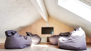 A room with a sloped ceiling, wooden walls, a flat-screen TV mounted on the wall, and three bean bags on the floor.