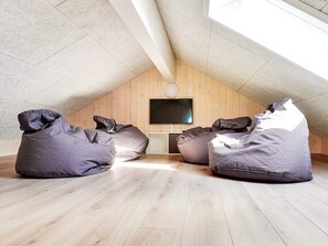 A room with a sloped ceiling, wooden walls, a flat-screen TV mounted on the wall, and three bean bags on the floor.
