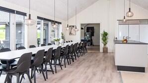 A modern dining area with a long table, chairs, pendant lights, and a kitchen island.