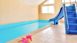 An indoor swimming pool with a blue slide and stairs, tiled walls, and a window.