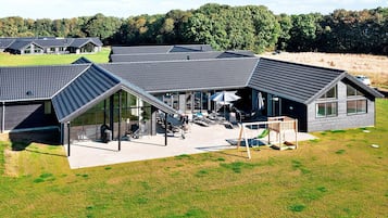 A modern building with a sloped roof, large windows, and a patio area with outdoor furniture.