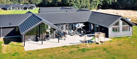 A modern building with a sloped roof, large windows, and a patio area with outdoor furniture.