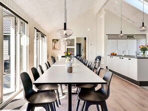 Un espace de salle à manger moderne avec une longue table, des chaises noires et des luminaires suspendus.