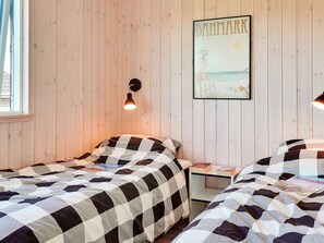 Two single beds with checkered bedding, a framed beach scene, and a table with a lamp.