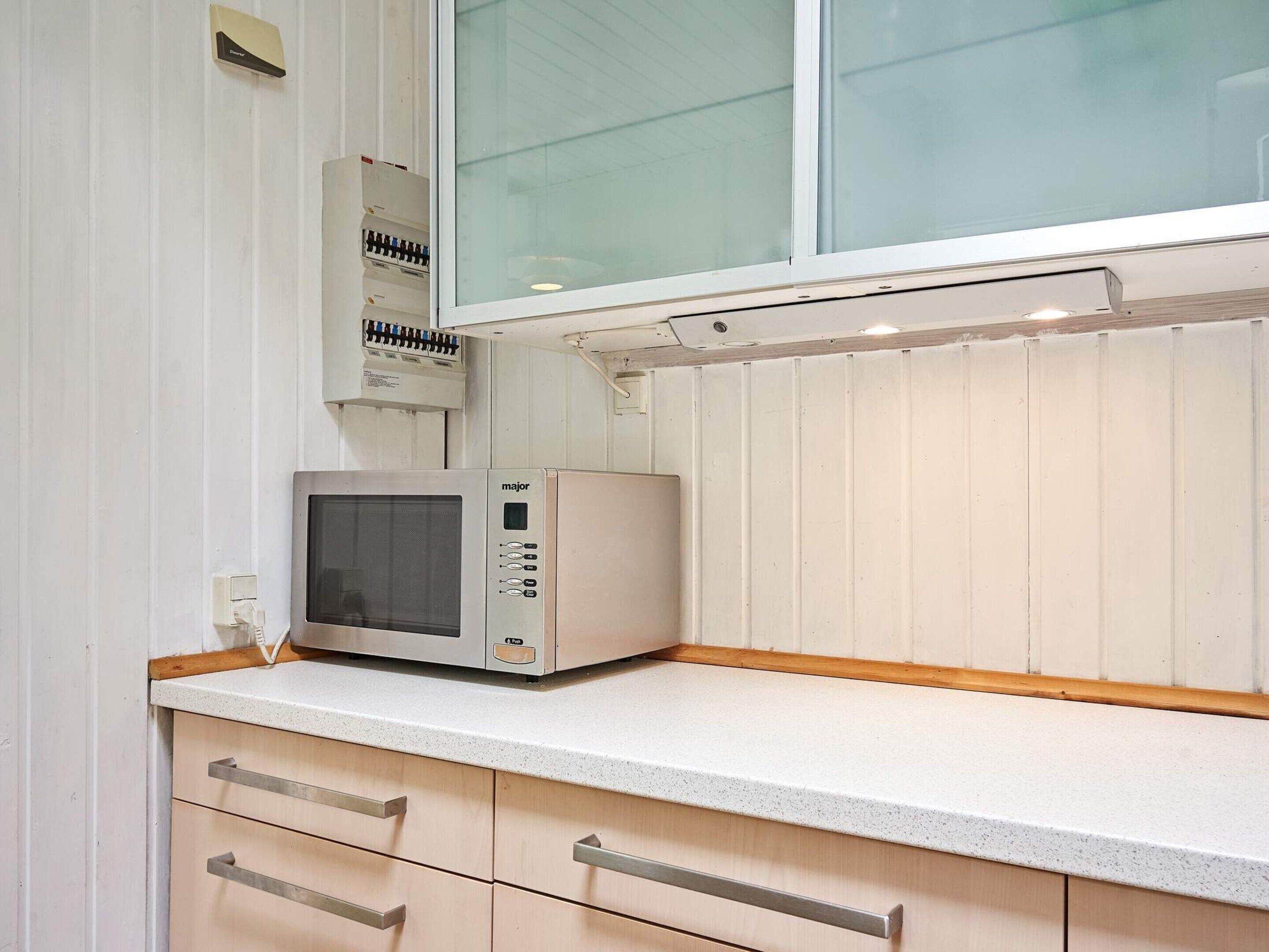A kitchen with a microwave on the countertop, wooden cabinets, and a window above.