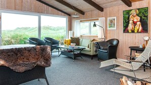 A cozy interior with a large window, wooden walls, and a mix of seating including a sofa, chairs, and a table.