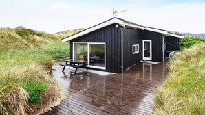 A modern black cabin with a deck, large windows, and a satellite dish.