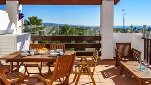 A terrace with a wooden table set for dining, surrounded by wooden chairs, overlooking a scenic landscape with mountains and greenery. - Coto Real by Interhome (Marbella)