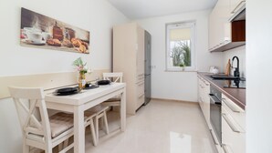 A compact kitchen with a dining table, chairs, a refrigerator, and a window.