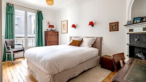 Ein Schlafzimmer mit einem großen Bett, einer Holzkommode, einem Sessel, einem Tisch und einem Kamin.
