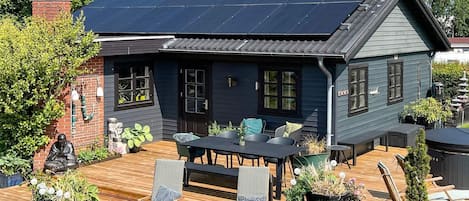 A house with a dark blue exterior, a solar panel roof, a wooden deck, and outdoor seating.