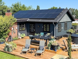 Een huis met een donkerblauwe gevel, een dak met zonnepanelen, een houten terras en buitenmeubels.