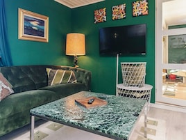 Una sala de estar con un sofá verde, una mesa de centro, una lámpara, un televisor y una silla.