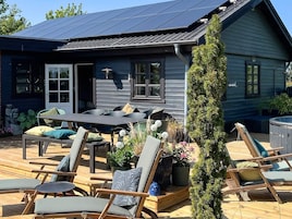Een houten terras met buitenmeubilair, een jacuzzi en een huis met zonnepanelen.