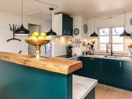 A kitchen with a wooden countertop, a bowl of fruit, hanging kitchen utensils, and a coffee machine.