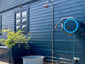 A blue house with a hose reel, a window, and a potted plant.
