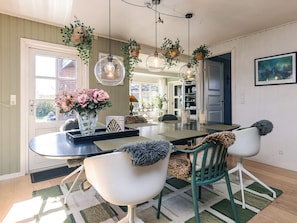 A dining area with a round table, chairs, hanging plants, and a pendant light.