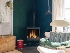 Et værelse med en brændeovn, en hvid stol med et blødt, grønt tæppe og en hængende lampe.