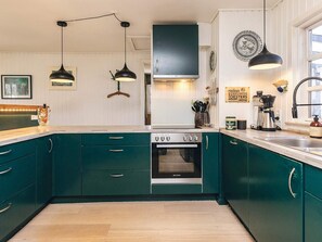 A kitchen with teal cabinets, a stove, and pendant lights. - 8 Person Holiday Home in Gilleleje (Gilleleje)
