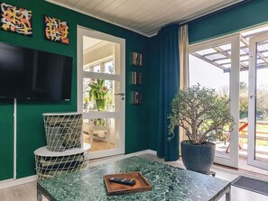 A room with a green wall, a television mounted on it, a door leading to a balcony, and a potted plant on the floor.