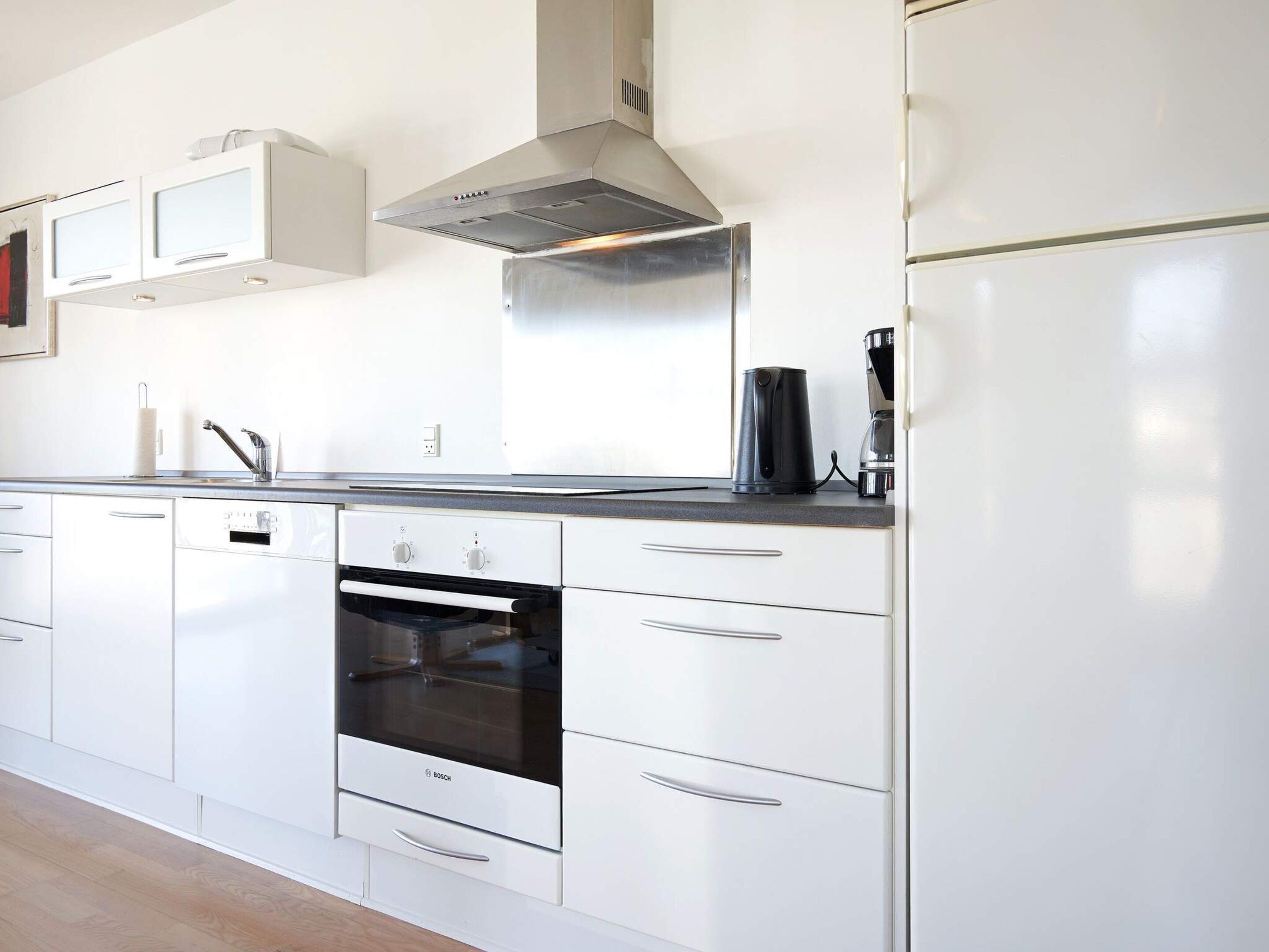 Una cocina moderna con armarios blancos, un horno Bosch, una campana extractora de acero inoxidable y una cafetera sobre la encimera.
