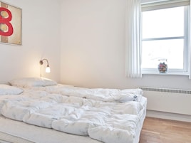 Un dormitorio con una cama, una lámpara de pared, una ventana con cortinas y una obra de arte en la pared.