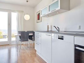 Una cocina moderna con lavavajillas incorporado, un comedor con mesa y sillas, y vistas a través de un ventanal.