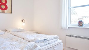Quarto com cama, mesa de cabeceira, relógio de parede, janela com vista e radiador.