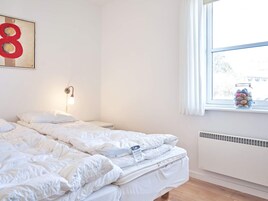 Un dormitorio con cama, luz empotrada en la pared, ventana con vistas y radiador.