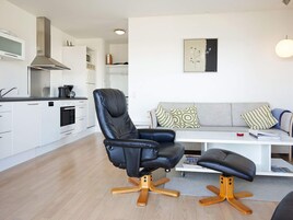 Una cocina moderna con armarios blancos, un sillón de cuero negro con patas de madera y un sofá gris con cojines estampados.