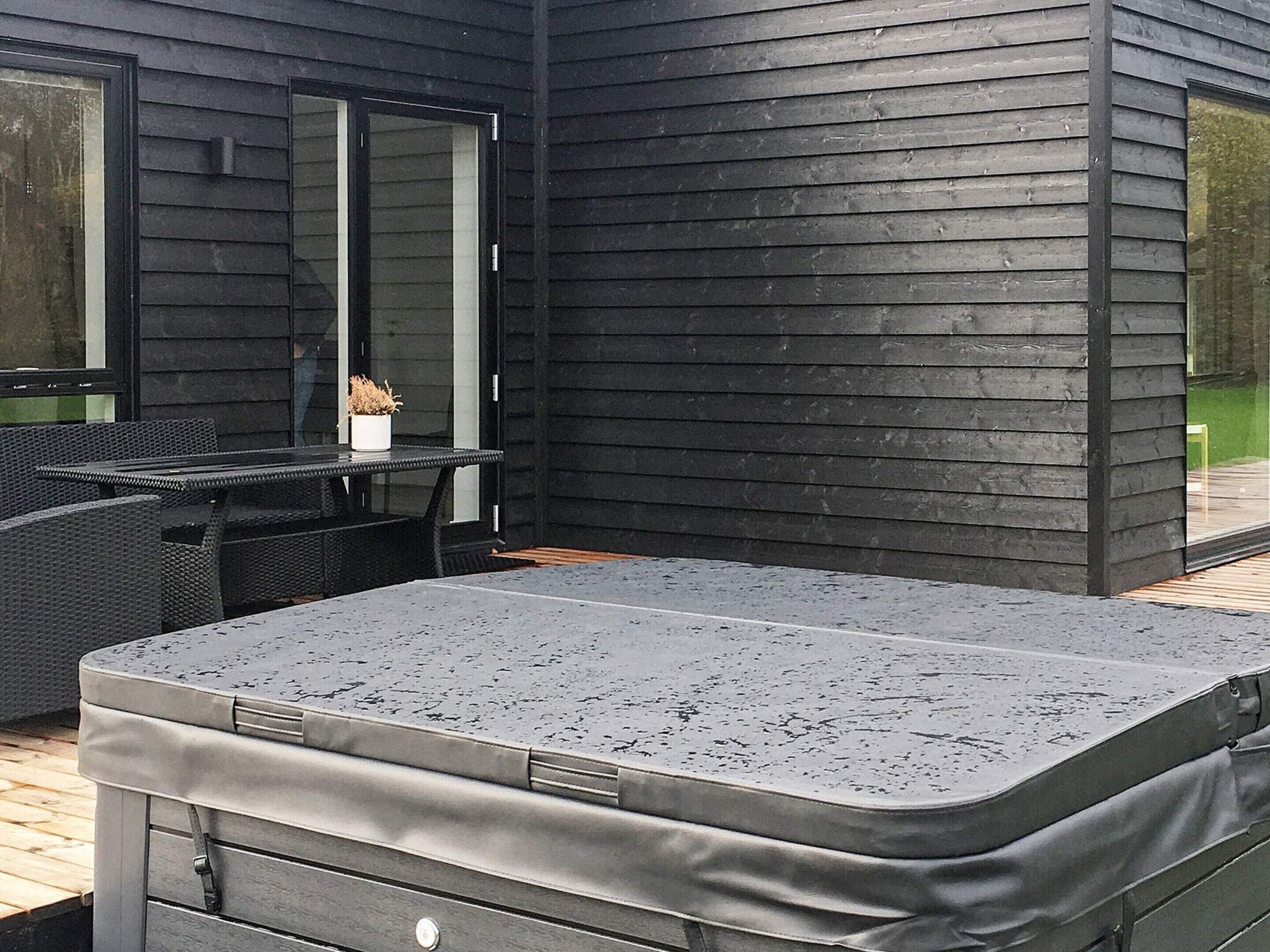 A modern outdoor seating area with a hot tub, wicker furniture, and a glass door leading to a patio.