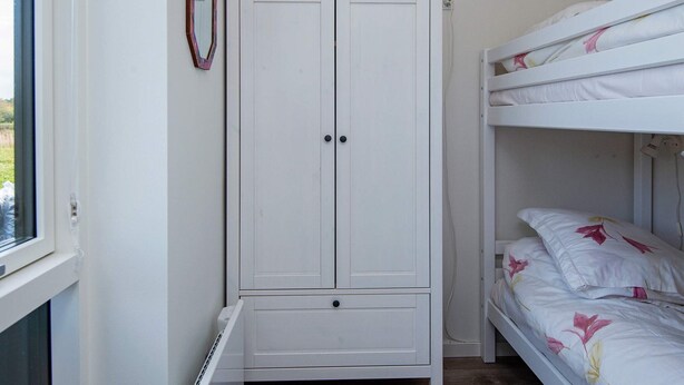 A room with a white wardrobe, a bed with floral bedding, and a window.