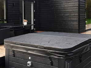Un jacuzzi exterior negro con superficie texturizada, una mesita con una planta en maceta y una silla de mimbre.
