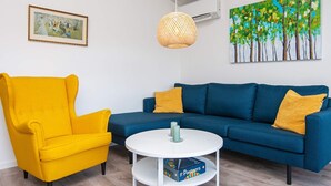 A living room with a blue sofa, a yellow armchair, a white coffee table, and a painting on the wall.