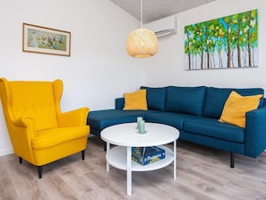 A living room with a blue sofa, a yellow armchair, a white coffee table, and a painting on the wall. - 5 Star Holiday Home in Ansager (Ansager)