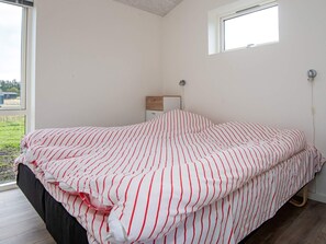 A bedroom with a bed, a nightstand, a window, and a view of the outdoors.